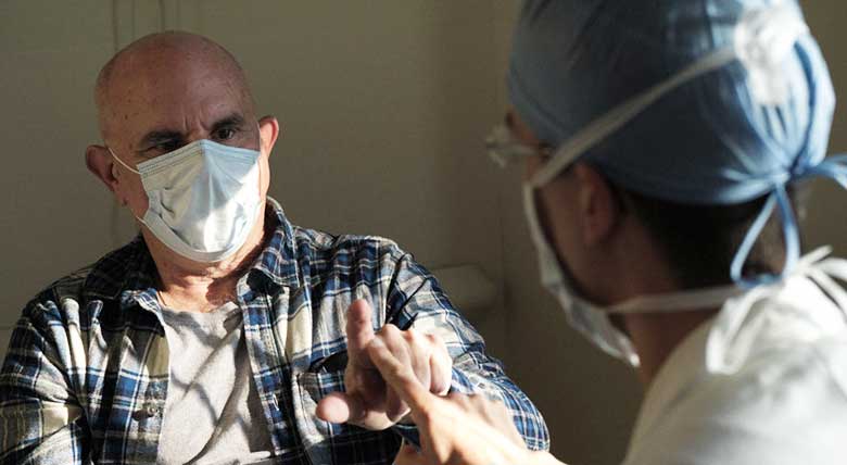 Older male patient in a mask reaching out to touch extended finger of doctor